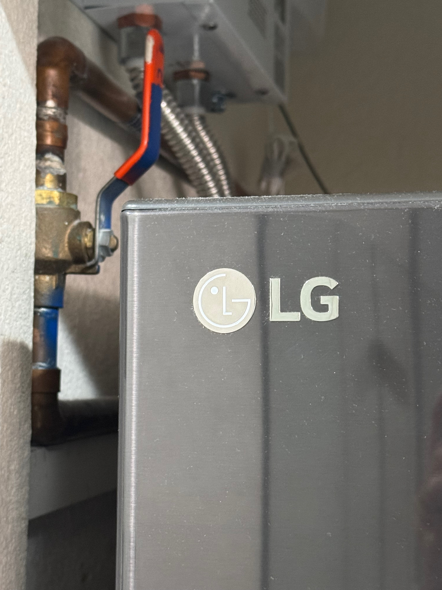 Orange water shut-off valve above the washer and dryer — vertical is on, horizontal is off
